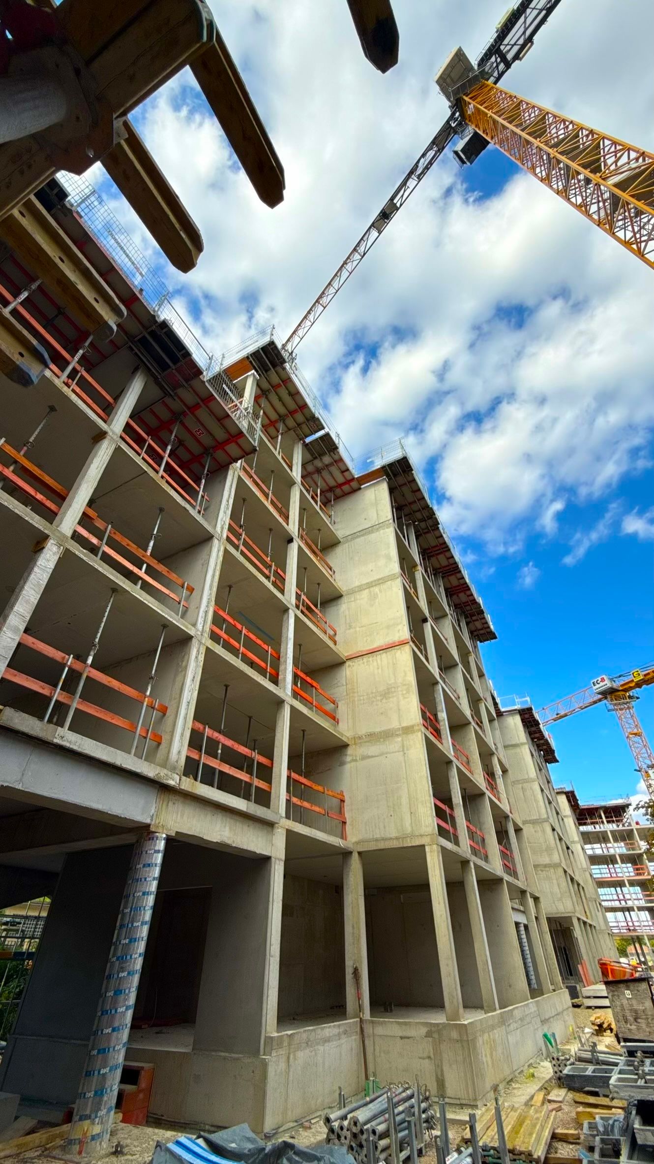 Rohbau eines mehrgeschossigen Gebäudes mit Betonstützen, Decken und Baukran.